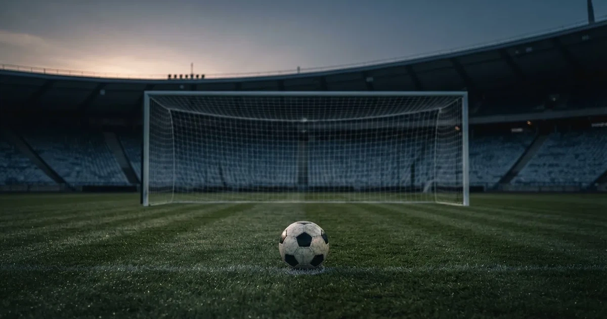 Ein Fußball liegt im Strafraum direkt vor dem Tor mit Netz, im Hintergrund leere Ränge bei Dämmerung.