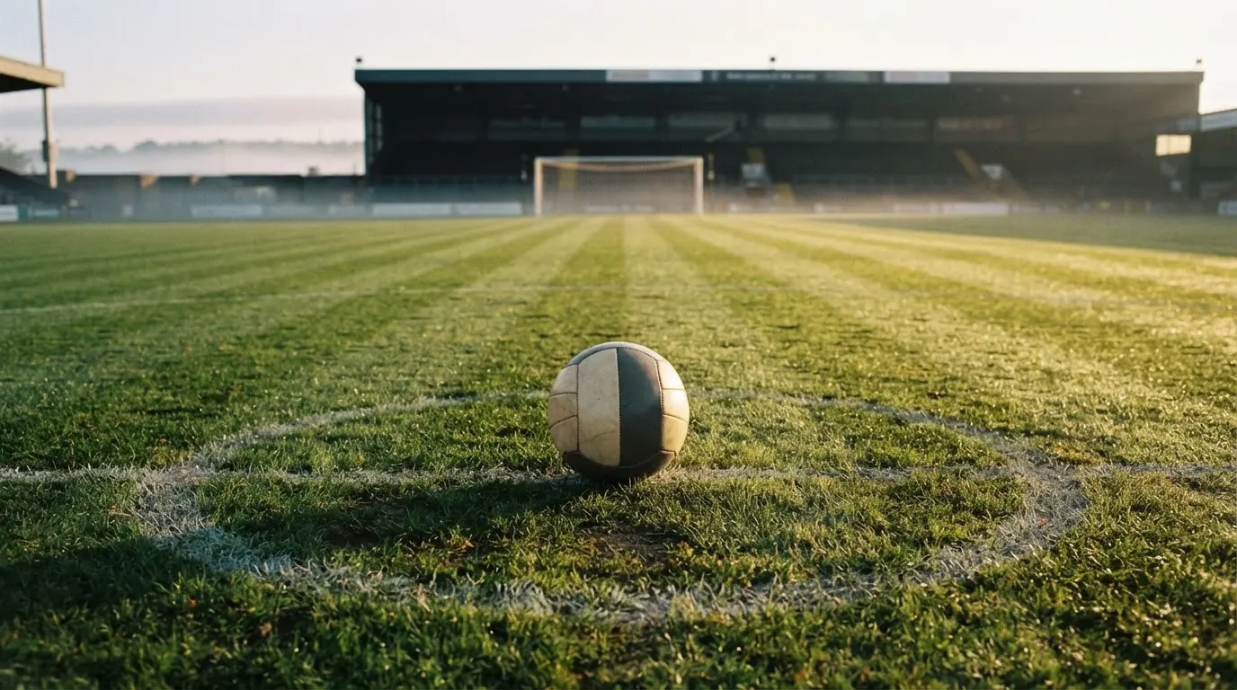 Ein Fußball auf dem Mittelkreis eines leeren Rasenplatzes im frühen Morgenlicht.