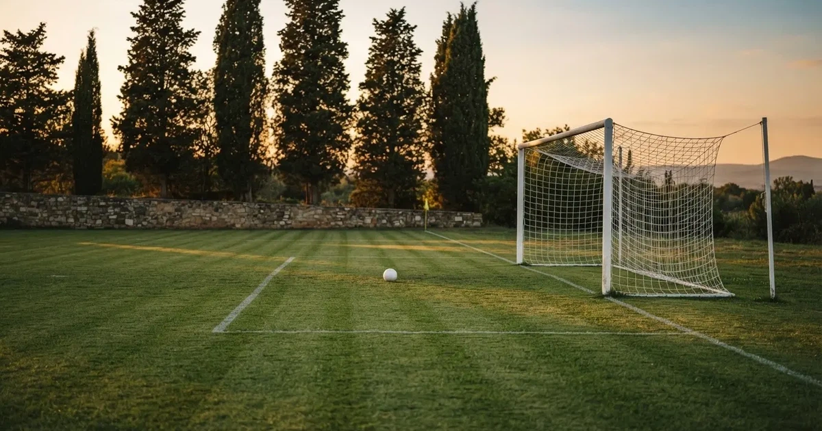 Ein Fußballtor mit Netz auf einem leeren Platz im Abendlicht, der Rasen frisch gemäht, im Hintergrund Zypressen.