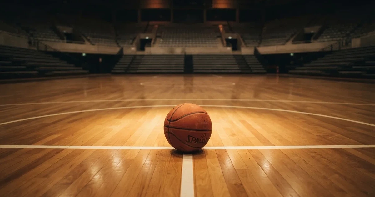 Ein Basketball liegt auf dem Parkettboden einer leeren Arena, Scheinwerfer werfen Licht auf die Mittellinie.