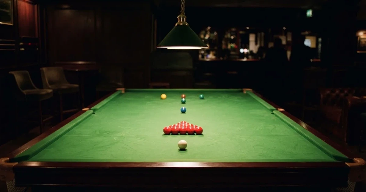 Ein Snookertisch mit grünem Tuch und aufgebauten roten Kugeln in einem abgedunkelten Raum unter einer hängenden Lampe.
