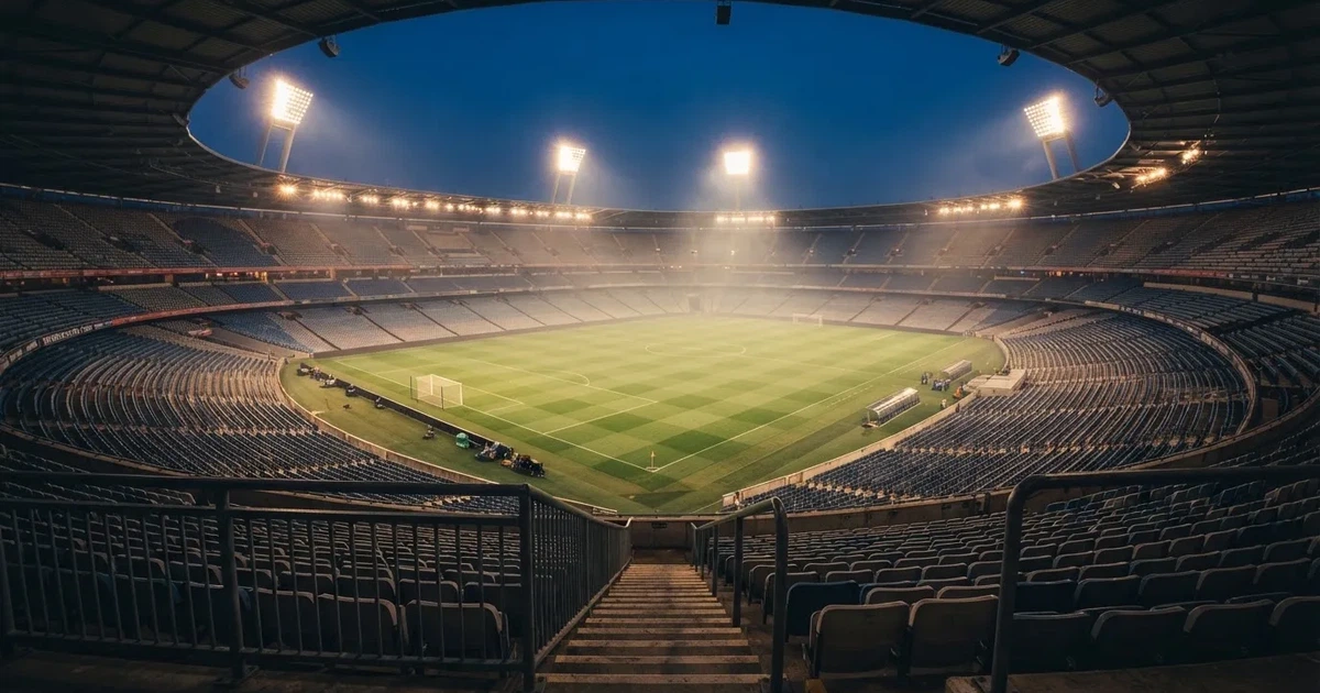 Ein leeres Stadion unter Flutlicht aus großer Entfernung gesehen, Dunst liegt über dem Rasen, die Tribünen sind nur als Lichtpunkte erkennbar.